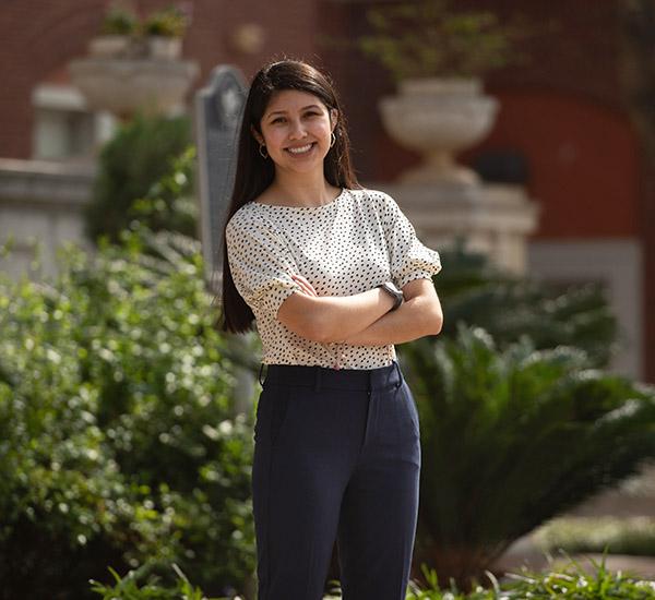 Smiling student posing with her arms crossed in front of the administration building